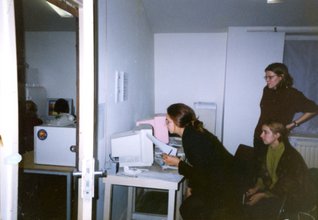 A photo of three women gathering around a desk with two vintage computers.