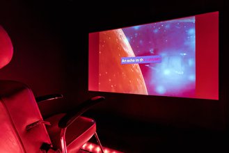 photogrpahy of an installation of a plush red chair facing a screen of space