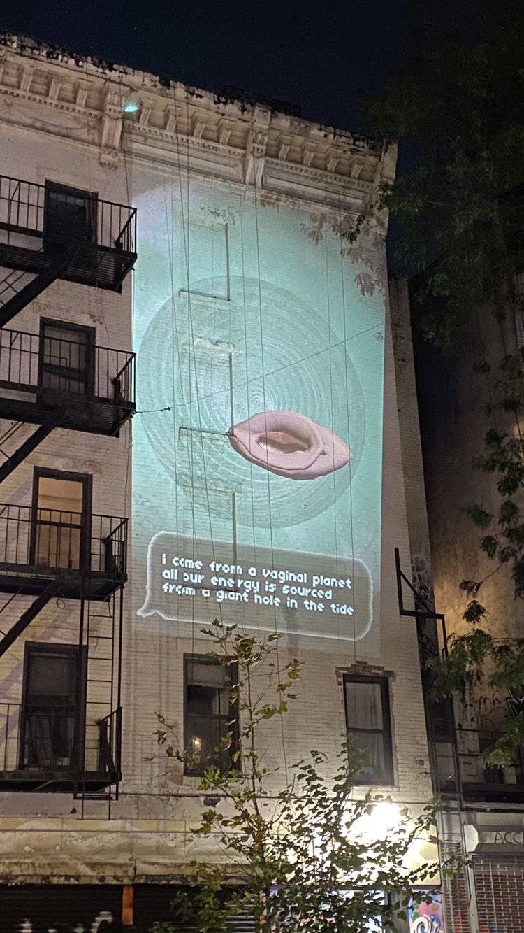 a photograph of the side of a building with a turquise projection with a pink vulva swirling in a vortex