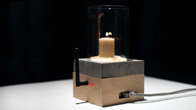 candle sitting on a box with silver plate with a router arm and red light on the side