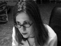 black and white screengrab of a white woman with shoulder length hair and glasses staring off to the side of a screen