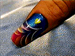 A finger with a colorful and vibrant nail of bold primary colors such as red, blue, and yellow in a fish scale or flower petals folding inwards pattern.