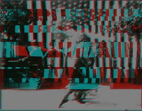 A black, cyan, red, and white glitched image of a dancer dancing to a man playing the piano outdoors. The American flag and its stars are almost subliminally scattered as the sky of the image.