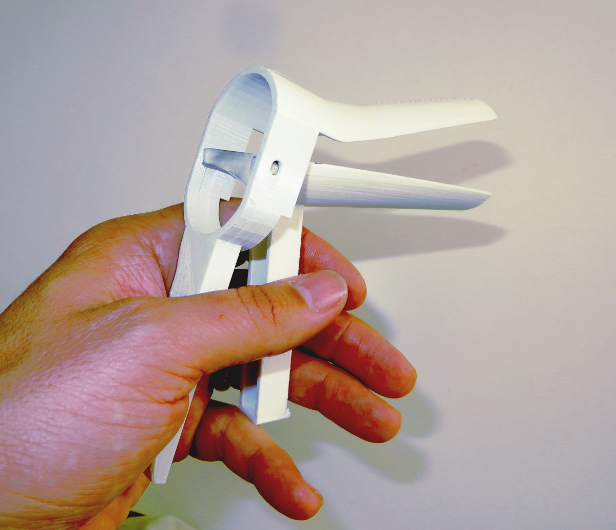 Photo of a hand holding a white device by the legs that opens and closes the contraption's mouth that looks like a pelican's beak.