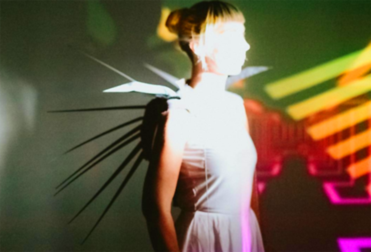 a blond woman in a white dress wears a back piece that resembles porcupine spikes