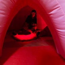 a women a VR headshet sitting inside a plush pink uterus with red light