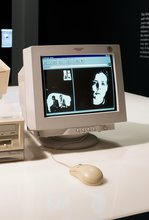 A vintage computer on a desk. The screen displays a retro webpage with a collage of two black & white images. The left shows two people sitting, the man faces his back towards the woman and she sits looking forward. The right shows a woman's face.