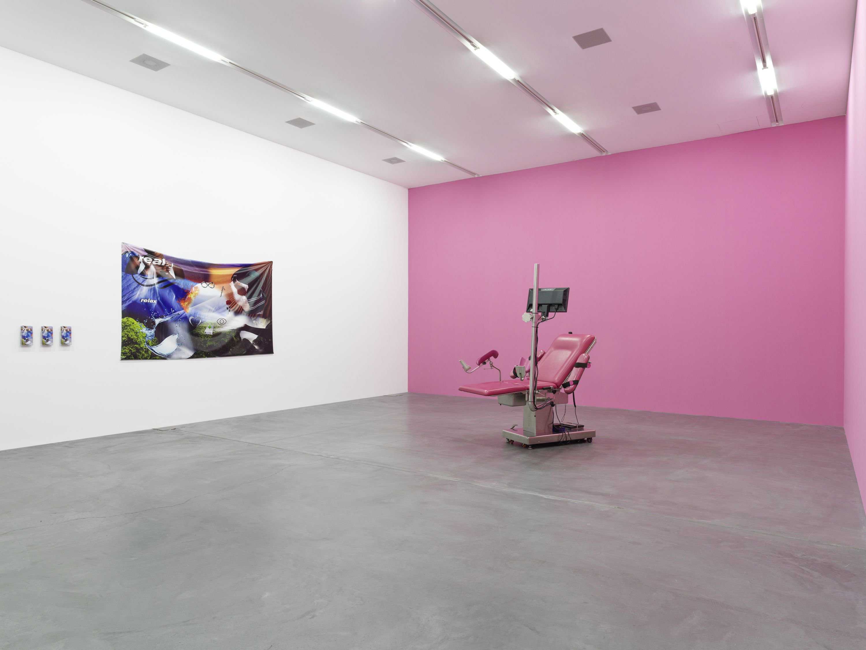 A gallery of a pink reclining dentist chair and a TV connected to it in front of a bright pink wall. To the left is a white wall with a tapestry showing images of nature and earthly spiritual elements collaged together.