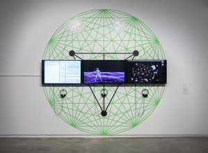 A gallery wall with three screens connected to headphones showing a document, a metallic man on a purple grid terrain, and scattered shapes. Behind is a large graphic green circle of a geometirc web behind a black triangle, lines connecting to vertices.