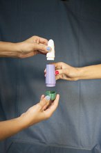 Two hands holding a plastic white cylindrical curved cone, a purple cylindrical shaft, and a green cap, displaying the different parts to the skeleton or container of a vibrator.