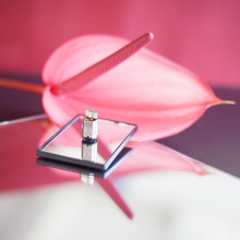 A commercial-like seductively elegant portrait of an exotic pink anthurium flower with a small metal device the size of a bullet sitting on a mirror bed stacked on a mirror plate.
