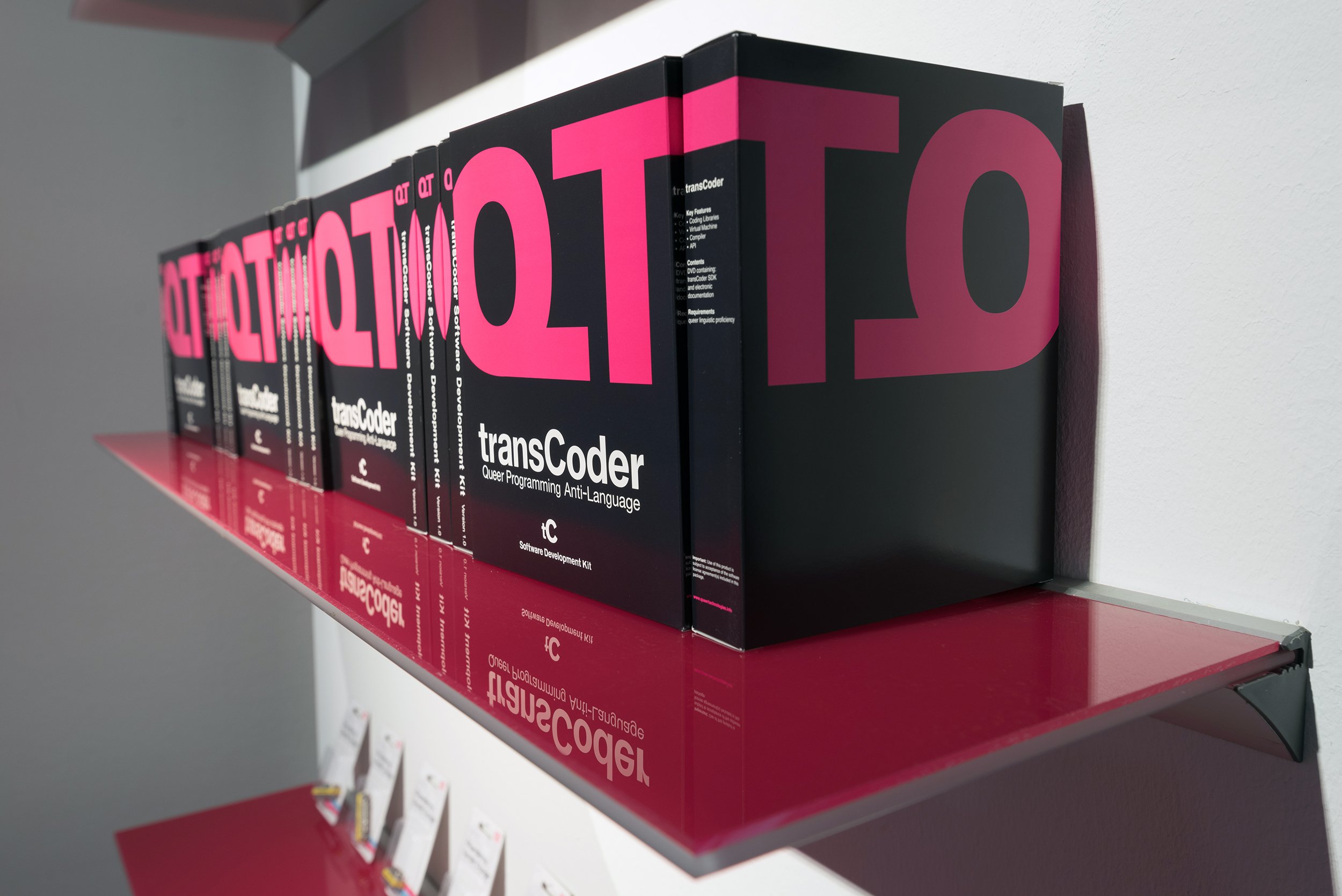 A red shelf with multiple boxes sitting next to each other. Each box is black with large pink QT printed on the top with a white “transCoder” below