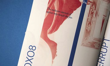A photo of a magazine page. It shows a vertical strip of inverted filtered upside down photograph of a person with long hair gazing away from the camera. "The exclusive interest of capital only benefit the few" typed in blue captions the image.